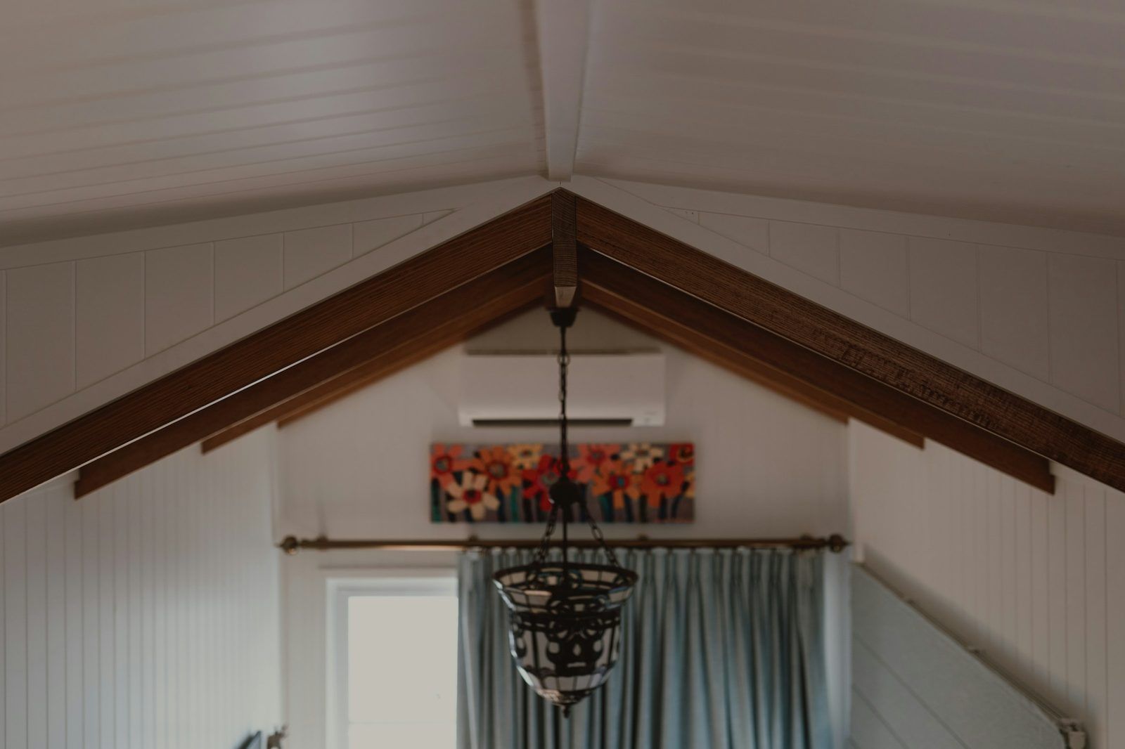 A vaulted room with a wall-mounted air conditioning unit above the window